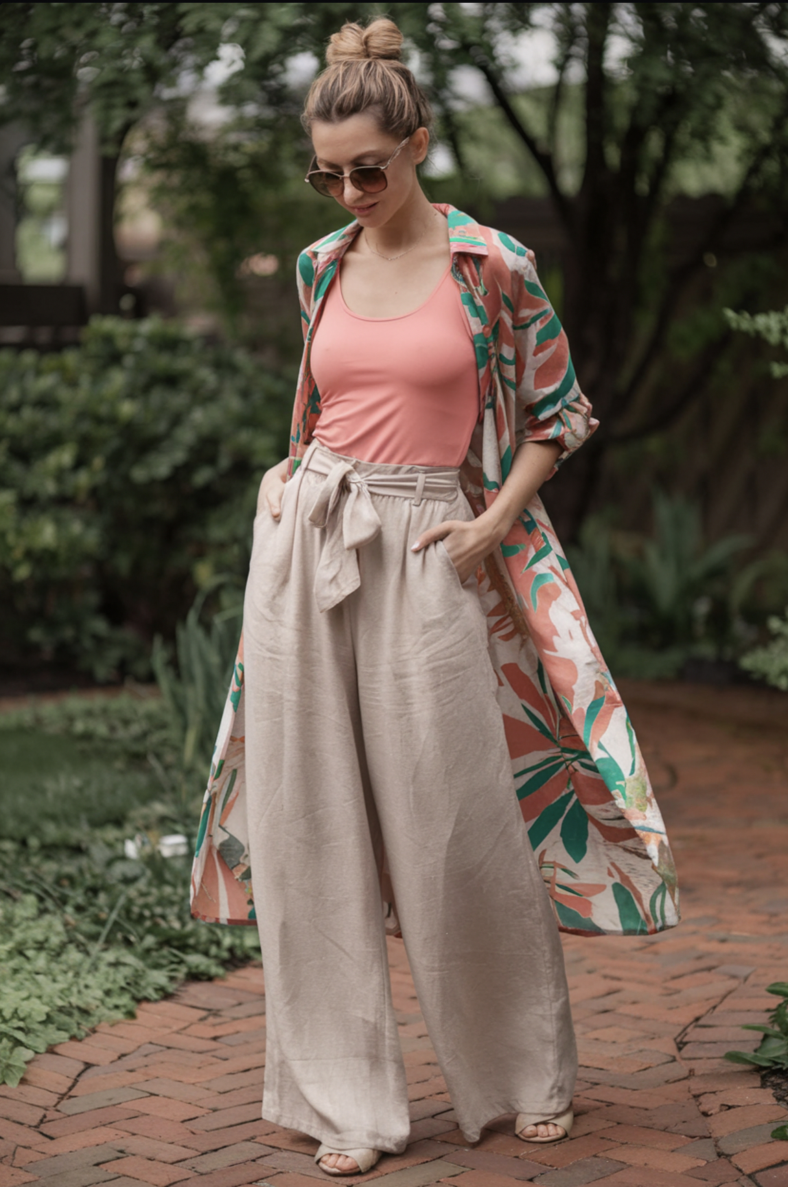 beige linen pants paired with a coral tank top and a tropical print duster